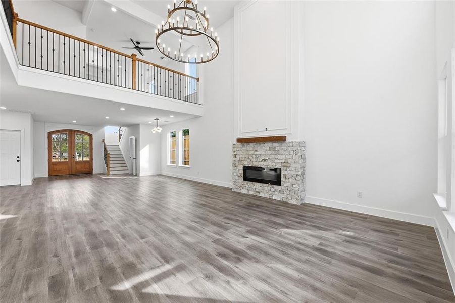 Unfurnished living room featuring a chandelier, stairs, a fireplace, wood finished floors, and a high ceiling