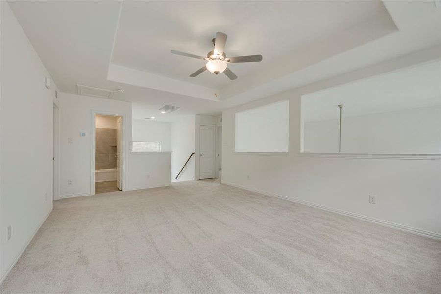 Unfurnished bedroom with light carpet, ensuite bathroom, ceiling fan, and a tray ceiling