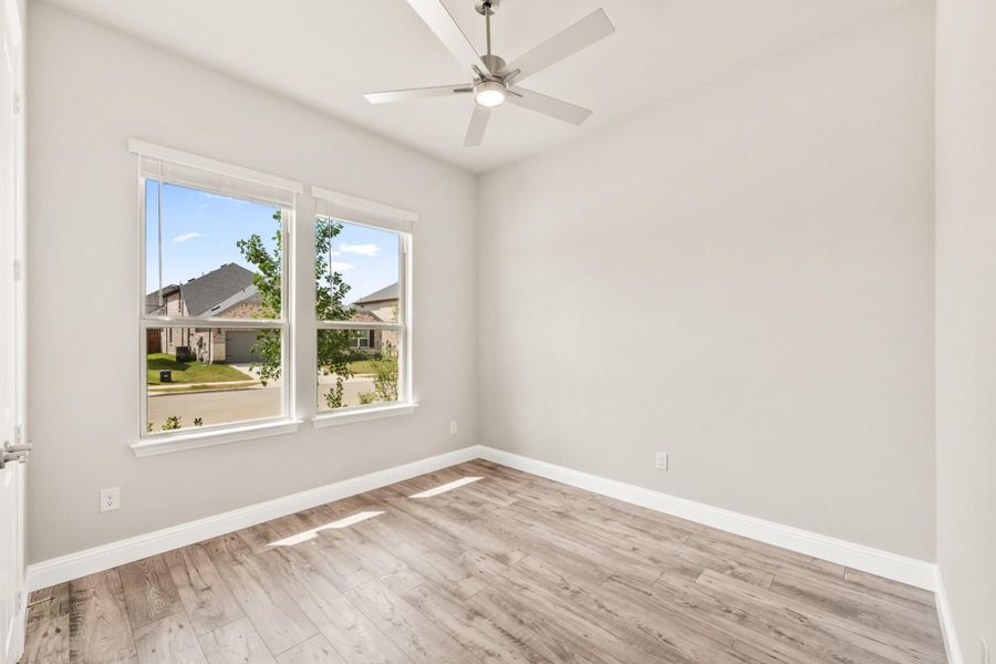 Empty bedroom with light wood floors, ceiling fan, and two windows overlooking a neighborhood street Empty bedroom with light wood floors, ceiling fan, and two windows overlooking a neighborhood street