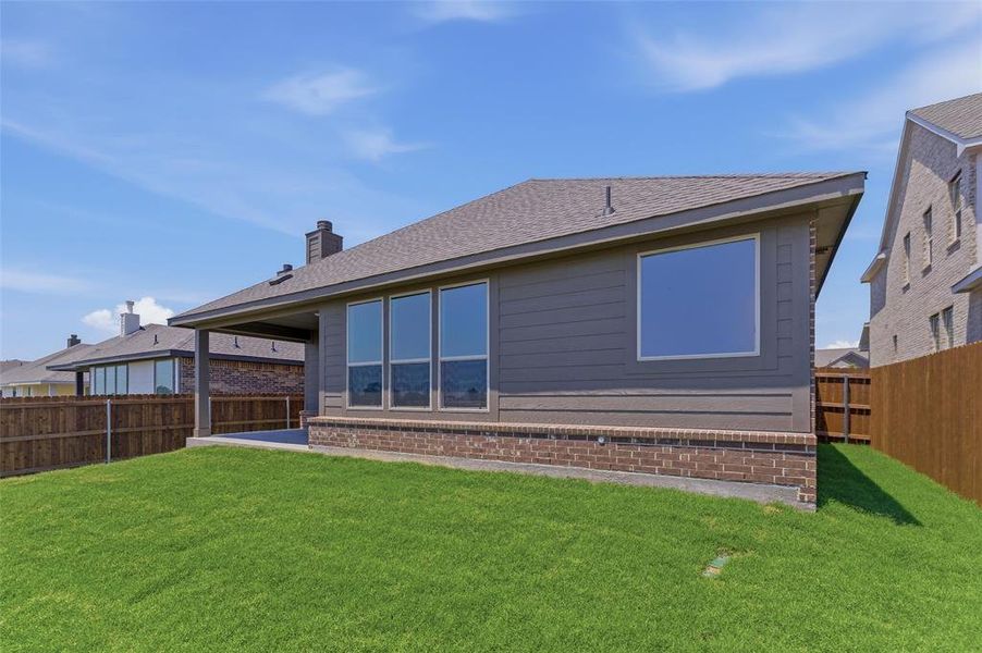 Expansive backyard featuring a manicured lawn, a covered patio, brick foundation, and multiple large windows on the rear elevation