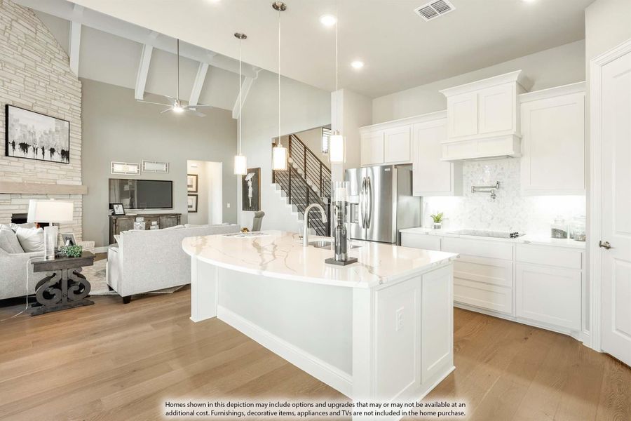 Open-concept kitchen with curved white island, vaulted ceiling, and view into living room with stone fireplace
