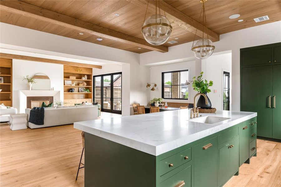Kitchen with green cabinetry, a chandelier, a center island with sink, a wooden ceiling with exposed beams, and light wood finished floors
