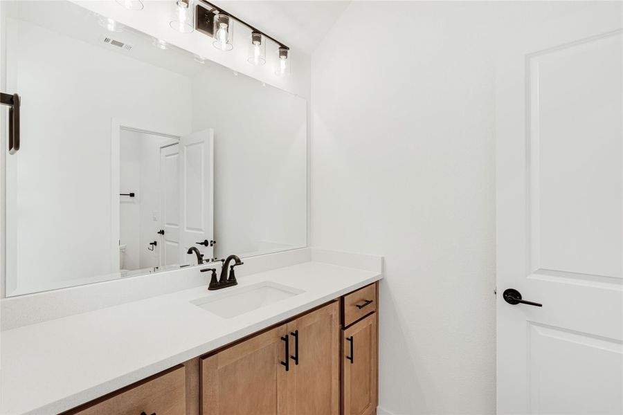 Bathroom vanity with wood cabinets, white countertop, large mirror, and black hardware fixtures Bathroom vanity with wood cabinets, white countertop, large mirror, and black hardware fixtures