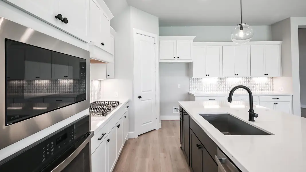 Kitchen featuring appliances with stainless steel finishes, pendant lighting, decorative backsplash, and white cabinets