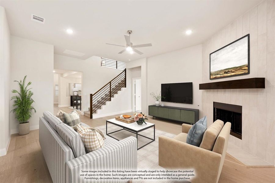 Living room with tile fireplace, hardwood floors, ceiling fan, and open staircase with metal railing