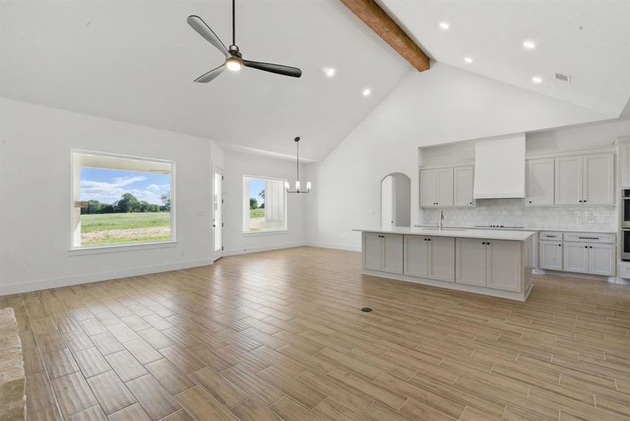 Unfurnished living room with high vaulted ceiling, ceiling fan, wood tiled floors, beam ceiling, and a chandelier Unfurnished living room with high vaulted ceiling, ceiling fan, wood tiled floors, beam ceiling, and a chandelier