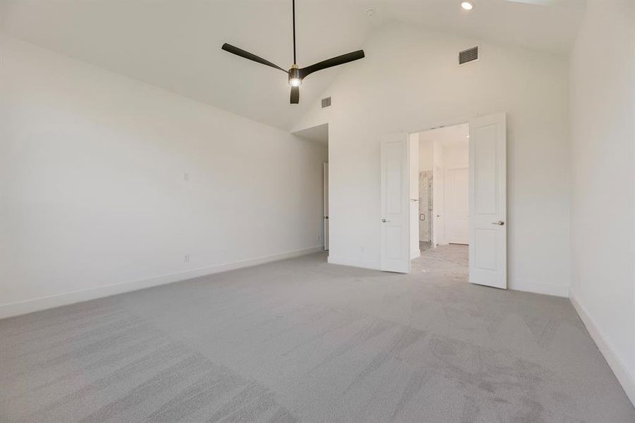 Unfurnished bedroom with light carpet, high vaulted ceiling, a ceiling fan, and connected bathroom