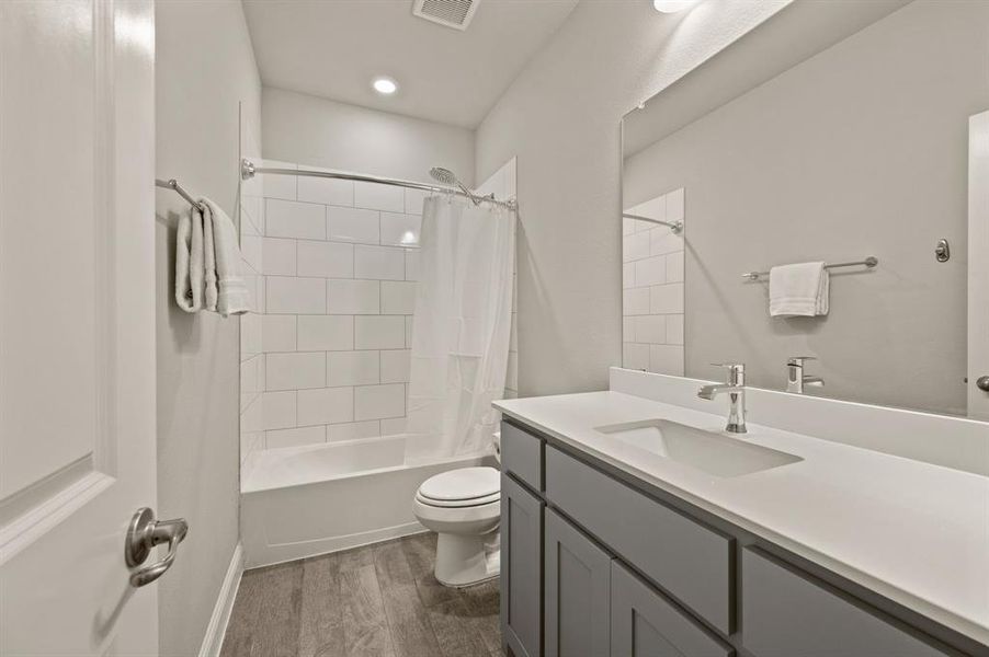 Full secondary bathroom with modern vanity, tile surround, and shower-tub combination.