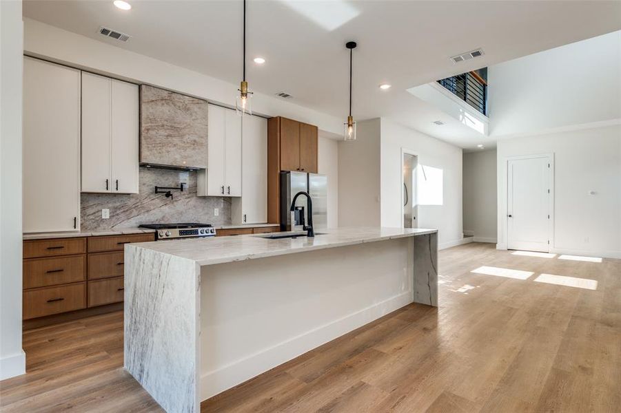 Kitchen with decorative light fixtures, light stone counters, backsplash, recessed lighting, and light wood-style flooring