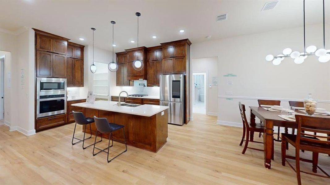 Kitchen with appliances with stainless steel finishes, light wood-style floors, light countertops, an island with sink, and recessed lighting