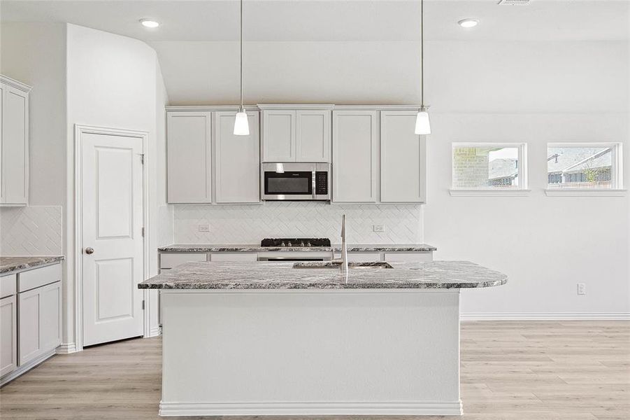 Kitchen with pendant lighting, range, a kitchen island with sink, light hardwood / wood-style floors, and decorative backsplash