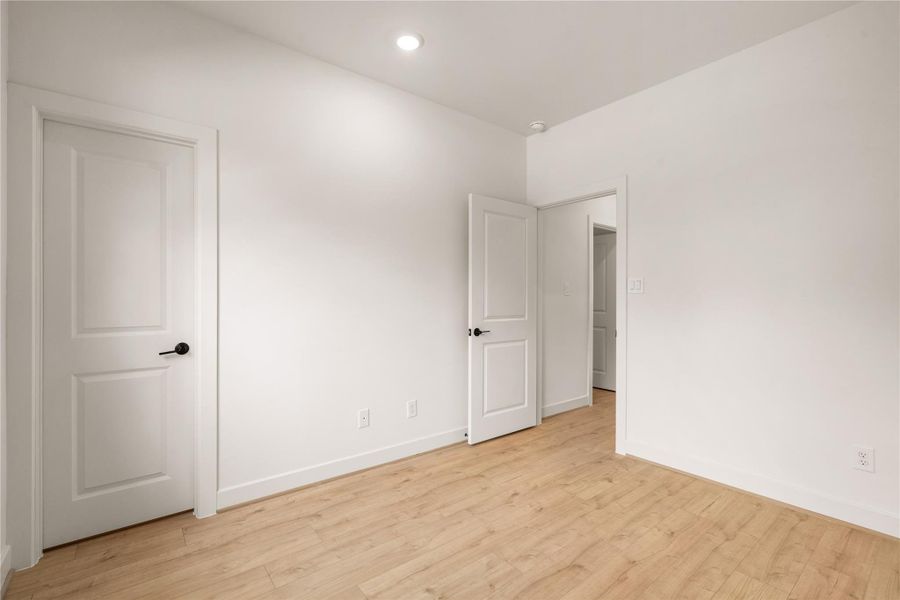 Bright guest bedroom perspective — smooth interior doors with matte black hardware, recessed lighting, and easy traffic flow to the hallway.