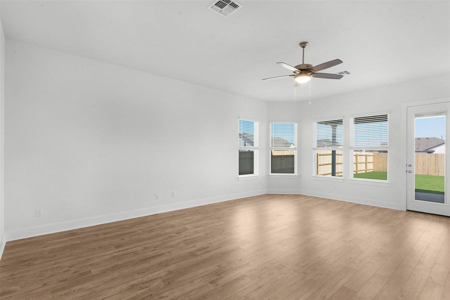 A spacious room offers light wood flooring, several windows, and a glass door leading to the backyard.