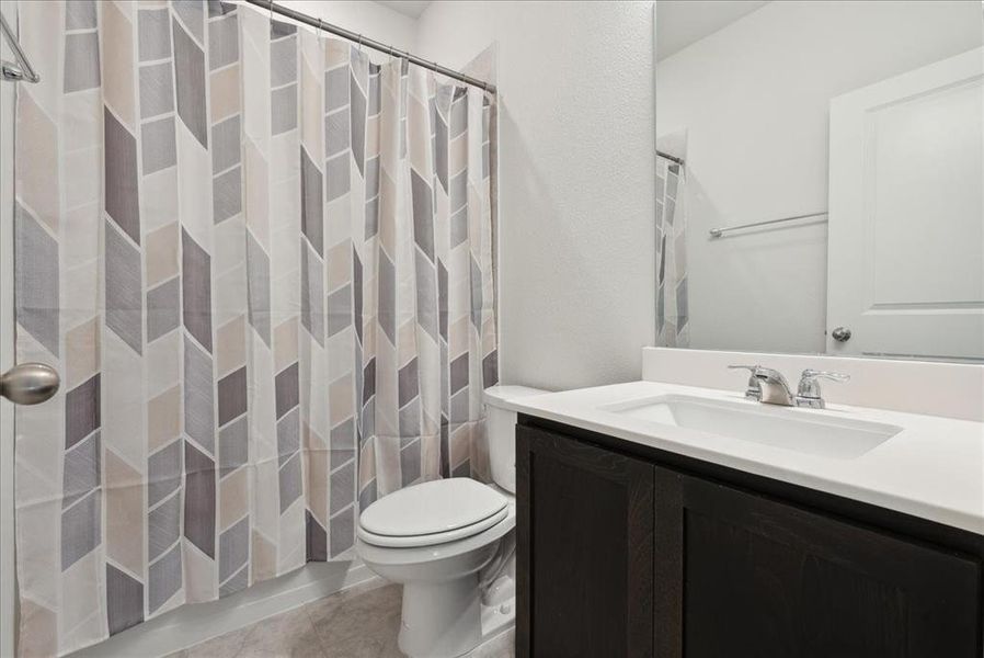 Bathroom with toilet, vanity, tile patterned floors, and a shower with shower curtain