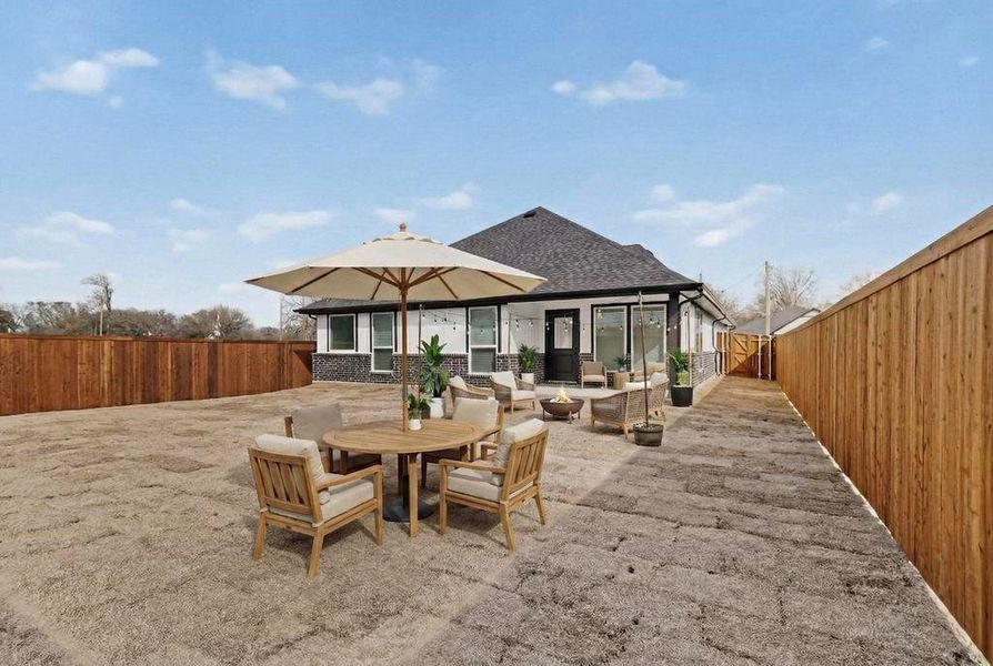 Rear view of house with a fenced backyard, a patio area, brick siding, outdoor dining space, and an outdoor fire pit