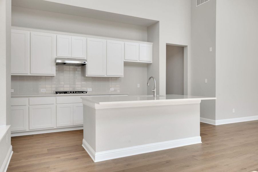 Kitchen featuring white cabinets, tasteful backsplash, light wood-style flooring, an island with sink, and light countertops