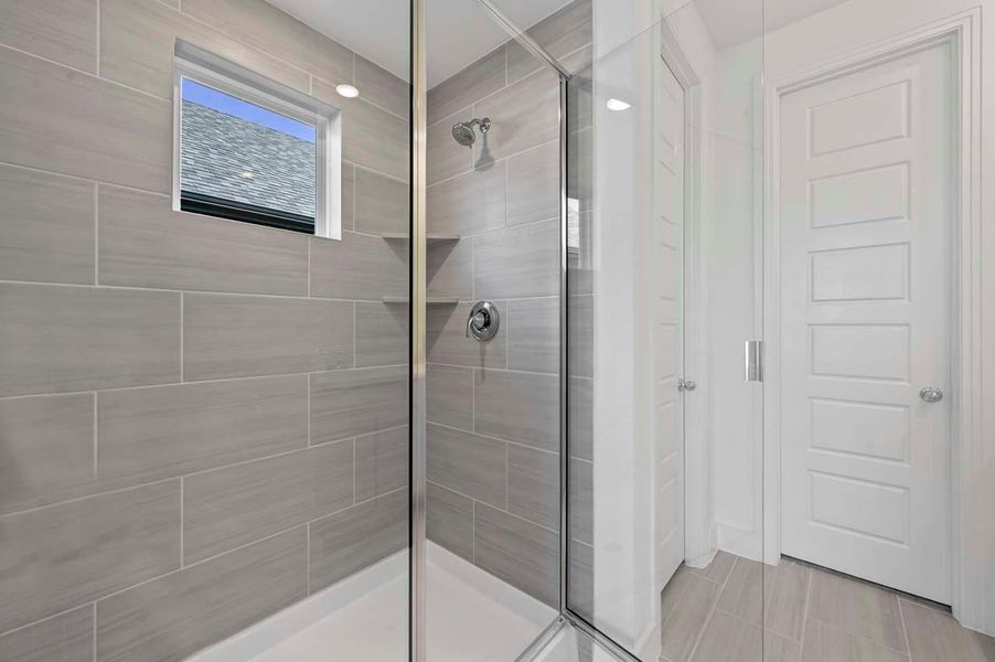 The primary bathroom features a spacious shower with a window above that brings in soft, natural light.