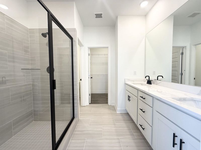Bathroom with a stall shower, double vanity, and a walk in closet