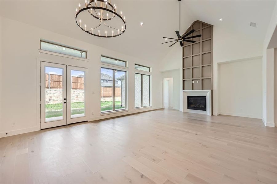 Unfurnished living room with french doors, light hardwood / wood-style flooring, a large fireplace, high vaulted ceiling, and ceiling fan with notable chandelier