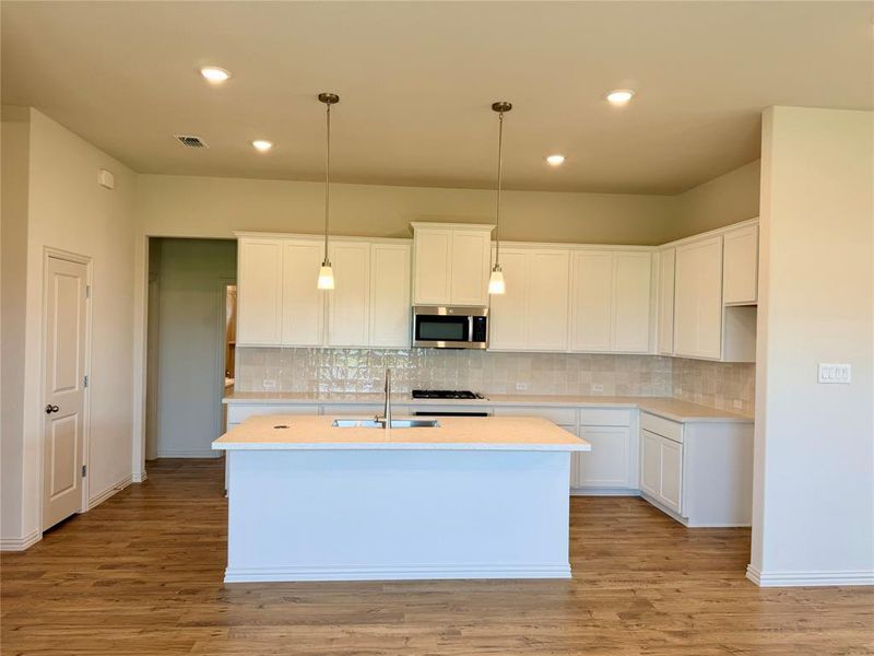 Kitchen featuring white cabinetry, a central island with a sink, stainless steel appliances, a tiled backsplash, and wood-finish flooring