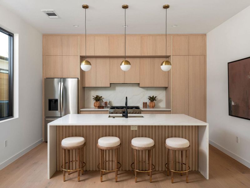 Kitchen with stainless steel fridge, hanging light fixtures, light stone counters, and a breakfast bar area