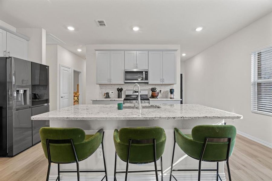 Kitchen with tasteful backsplash, appliances with stainless steel finishes, light wood-style flooring, light stone countertops, and a breakfast bar Kitchen with tasteful backsplash, appliances with stainless steel finishes, light wood-style flooring, light stone countertops, and a breakfast bar