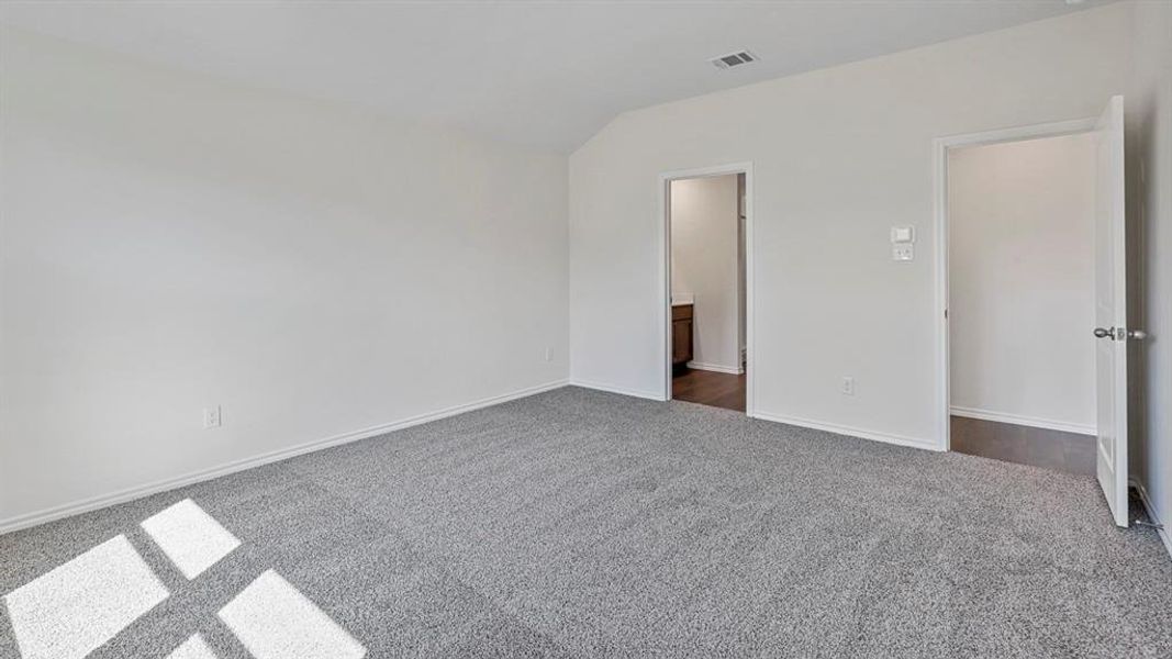 Unfurnished bedroom with dark carpet, connected bathroom, and lofted ceiling Unfurnished bedroom with dark carpet, connected bathroom, and lofted ceiling