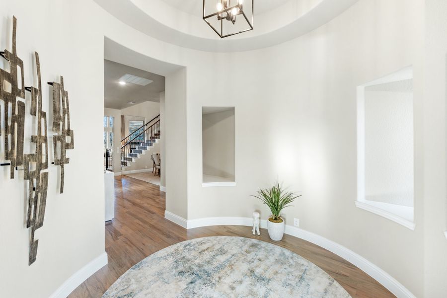 Curved foyer with tray ceiling, pendant light, hardwood floors, and staircase visible in background Curved foyer with tray ceiling, pendant light, hardwood floors, and staircase visible in background