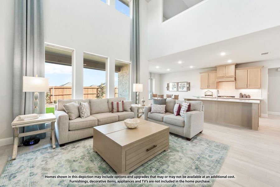 Open-concept living room with two-story ceiling, large windows, two sofas, and kitchen visible in background.