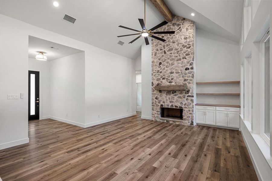 iving room with beamed ceiling, a stone fireplace, light wood finished floors, high vaulted ceiling, and ceiling fan