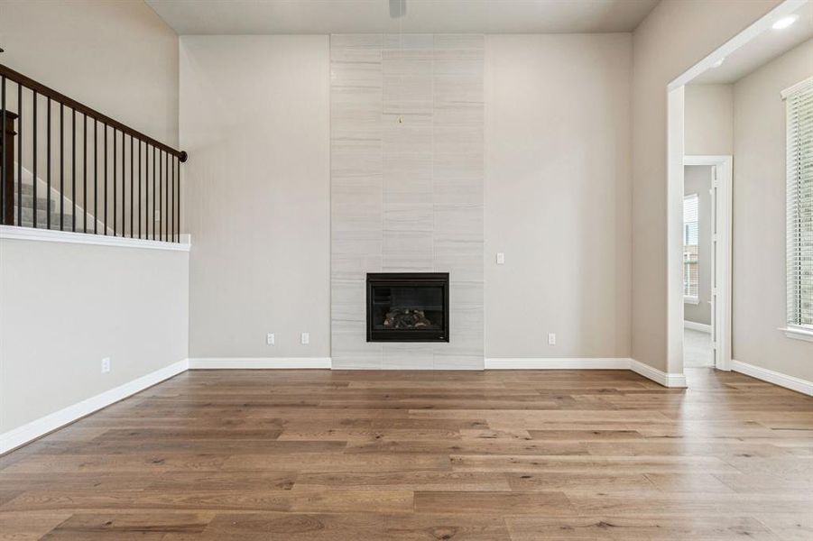 Unfurnished living room with wood finished floors, a tiled fireplace, and a ceiling fan