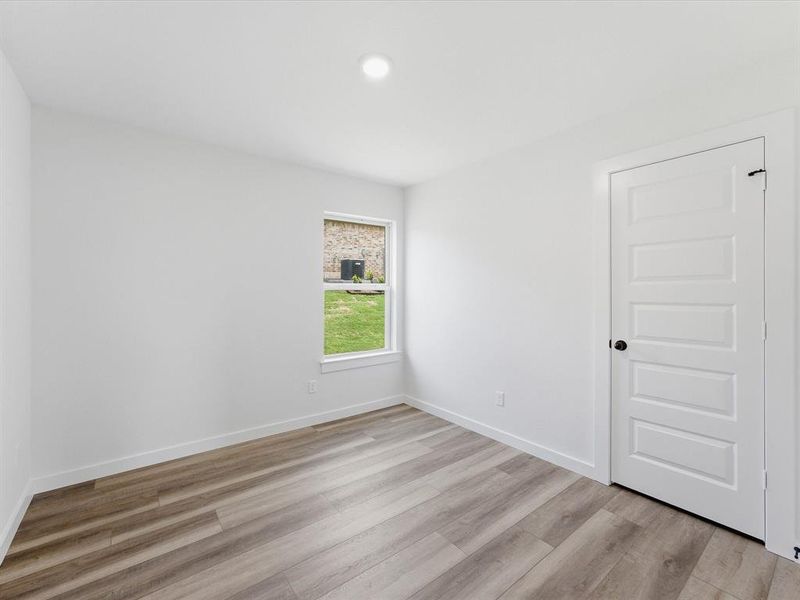 Neutral palette room featuring wood-finish flooring, white trim, and a window overlooking a green lawn Neutral palette room featuring wood-finish flooring, white trim, and a window overlooking a green lawn
