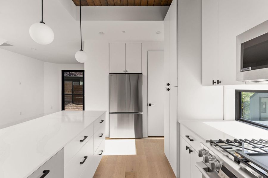 Kitchen featuring stainless steel appliances, decorative light fixtures, white cabinetry, light wood-type flooring, and light stone counters