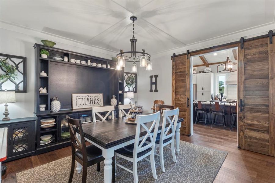 Charming dining area featuring rich wood flooring, tray ceiling detail, statement lighting, built-in display storage, and rustic sliding barn doors that connect beautifully to the kitchen.