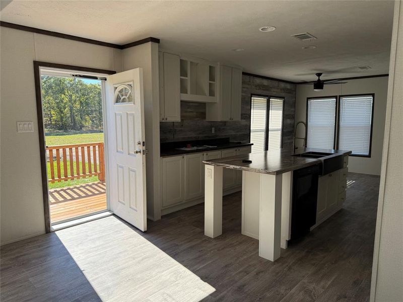 Kitchen with dark wood-type flooring, a kitchen island with sink, white cabinetry, dark countertops, and ornamental molding