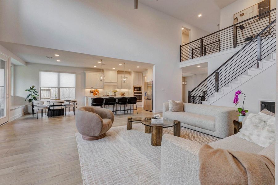 This spacious living area features an open floor plan with high ceilings and modern design. The kitchen boasts sleek cabinetry and a large island with seating. A cozy living room and dining area are well-lit by natural light from large windows. An elegant staircase leads to the upper level, adding sophistication to the space. This spacious living area features an open floor plan with high ceilings and modern design. The kitchen boasts sleek cabinetry and a large island with seating. A cozy living room and dining area are well-lit by natural light from large windows. An elegant staircase leads to the upper level, adding sophistication to the space.