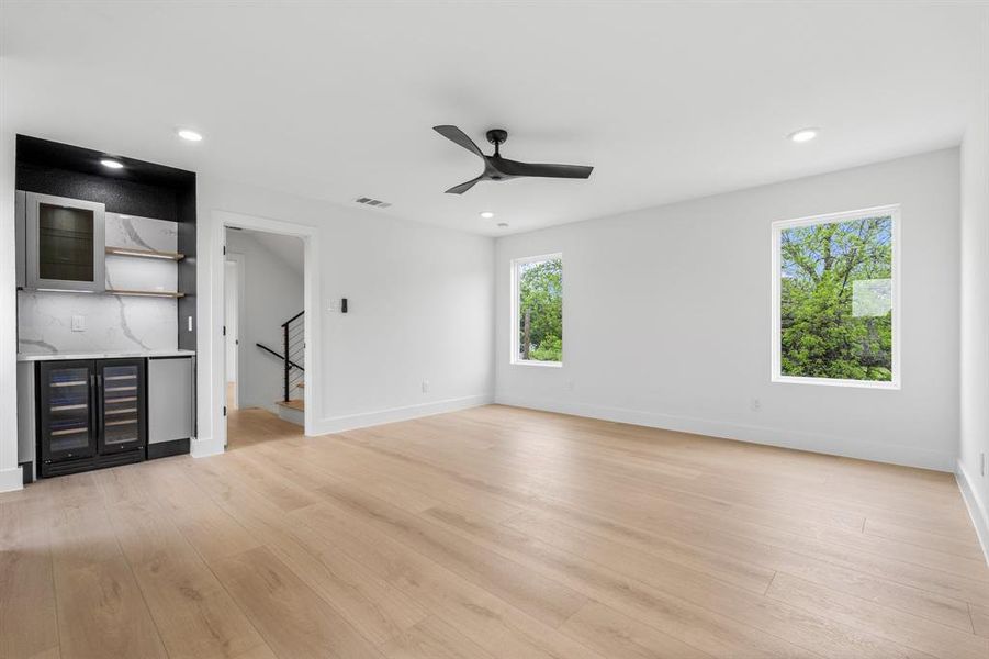Unfurnished living room with bar area, light wood-type flooring, visible vents, a ceiling fan, and stairs