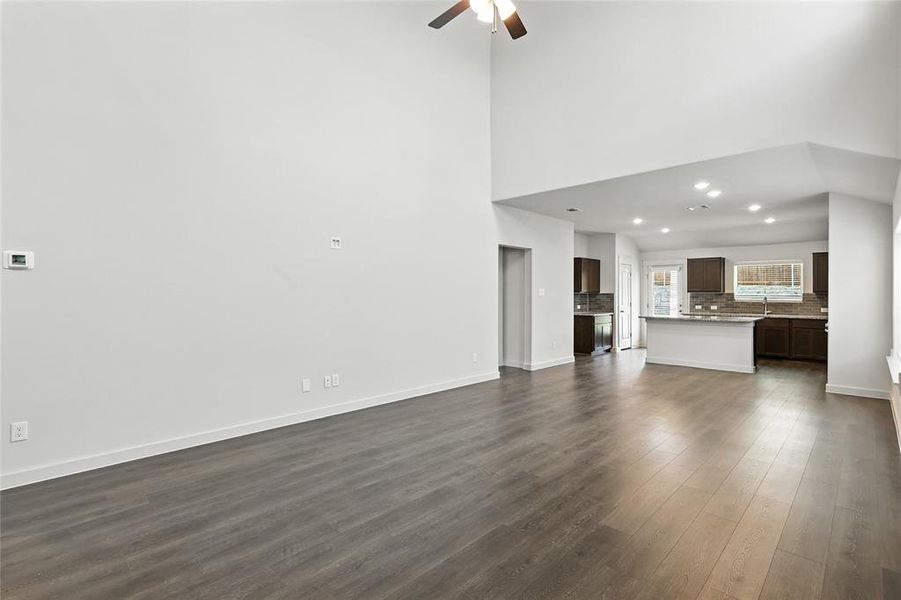Unfurnished living room with dark wood-style flooring, a ceiling fan, recessed lighting, and a towering ceiling Unfurnished living room with dark wood-style flooring, a ceiling fan, recessed lighting, and a towering ceiling