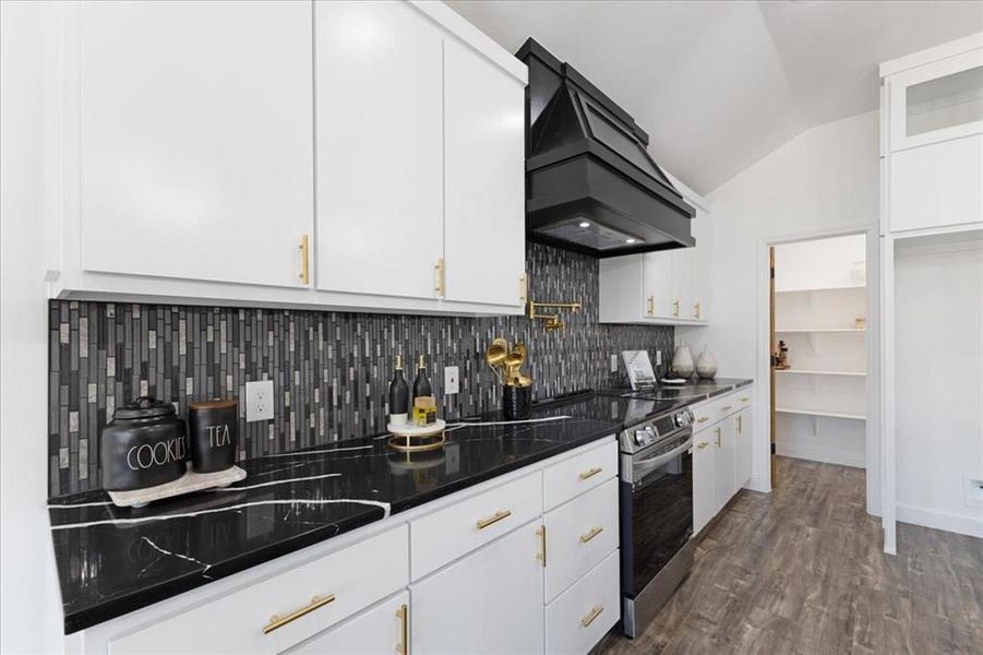 Kitchen with white cabinets, vaulted ceiling, dark wood finished floors, glass insert cabinets, and custom range hood