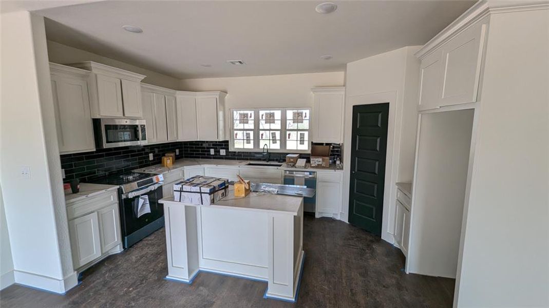 Kitchen with light countertops, decorative backsplash, white cabinets, stainless steel appliances, and a sink