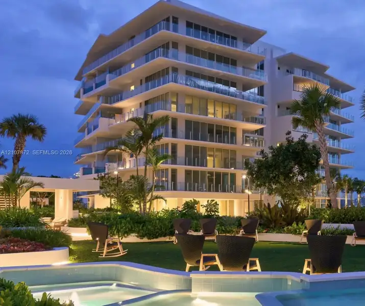 Mid-rise building exterior featuring tiered balconies with glass railings, an outdoor water feature with stone coping, and manicured landscaping Mid-rise building exterior featuring tiered balconies with glass railings, an outdoor water feature with stone coping, and manicured landscaping
