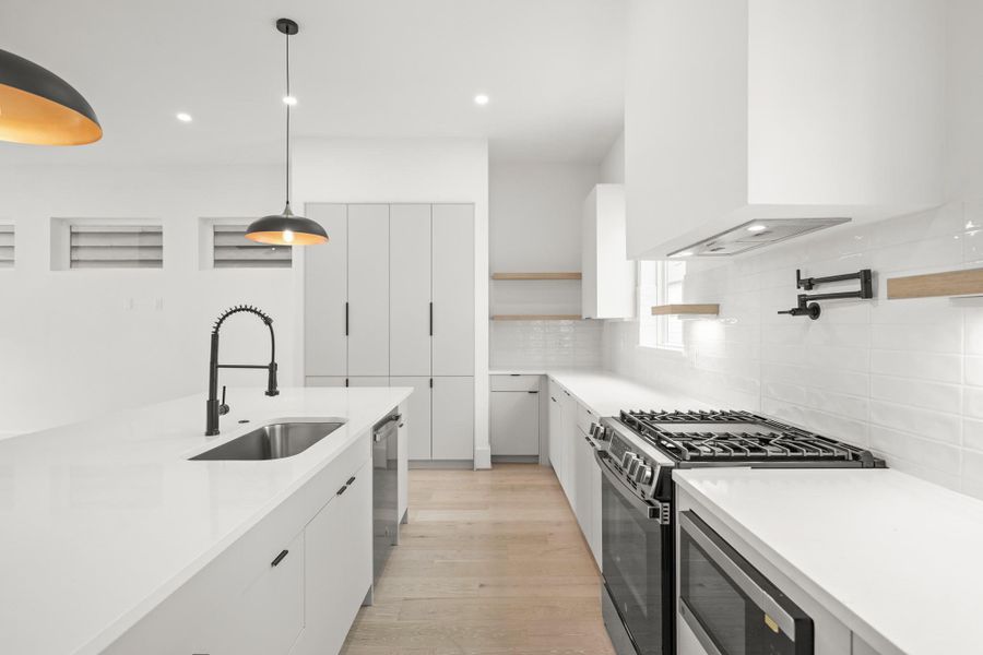 A wall-mounted pot filler adds convenience, while the GE microwave integrates seamlessly into the cabinetry. The large island features a stainless steel sink with sleek black faucet, combining style and function. Together, these modern appliances make cooking convenient and effortless. To the back right is the perfect spot for a coffee bar!