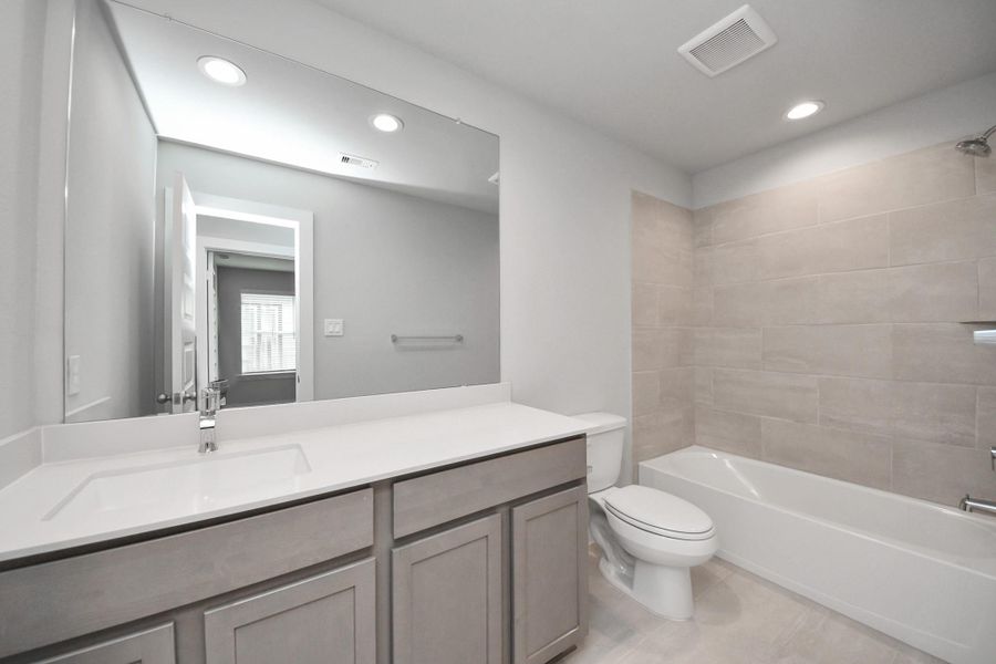 Secondary bath features tile flooring, bath/shower combo with tile surround, light stained wood cabinets, beautiful light countertop.