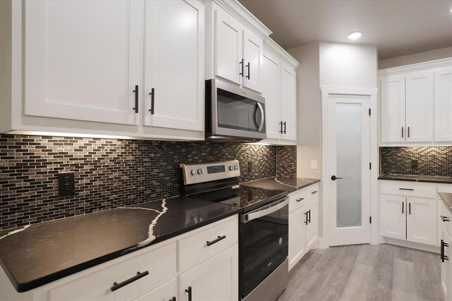 Kitchen with light hardwood / wood-style flooring, stainless steel appliances, dark stone counters, white cabinetry, and tasteful backsplash