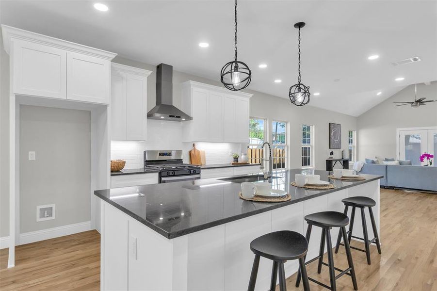 Kitchen with white cabinets, wall chimney exhaust hood, stainless steel range with gas cooktop, open floor plan, and tasteful backsplash