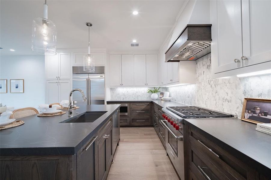 Kitchen featuring decorative light fixtures, high quality appliances, sink, white cabinets, and a kitchen island with sink