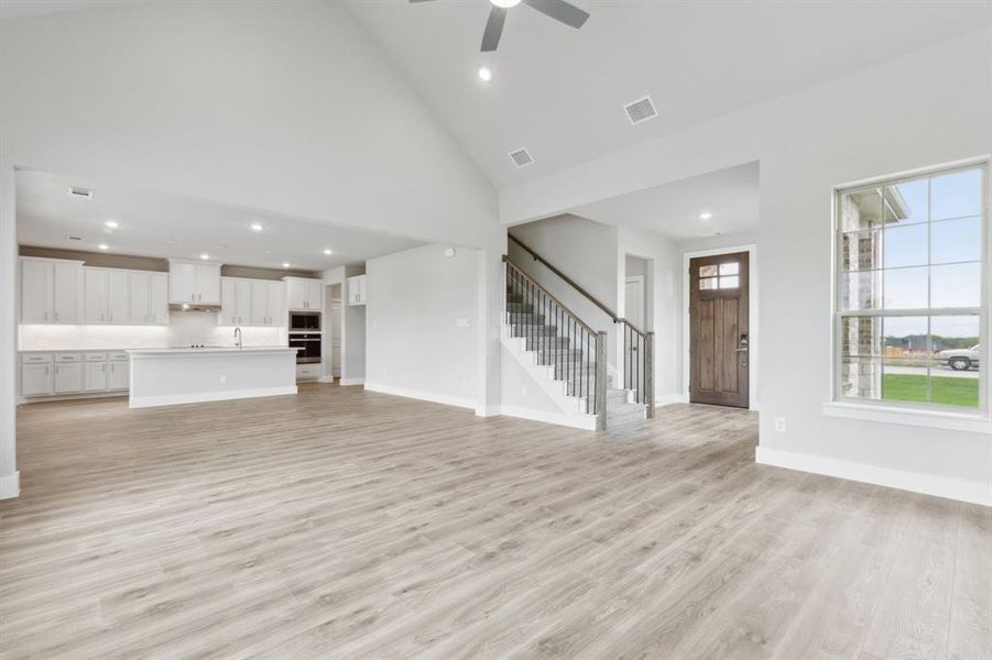 Unfurnished living room featuring high vaulted ceiling, recessed lighting, stairs, light wood finished floors, and a ceiling fan Unfurnished living room featuring high vaulted ceiling, recessed lighting, stairs, light wood finished floors, and a ceiling fan