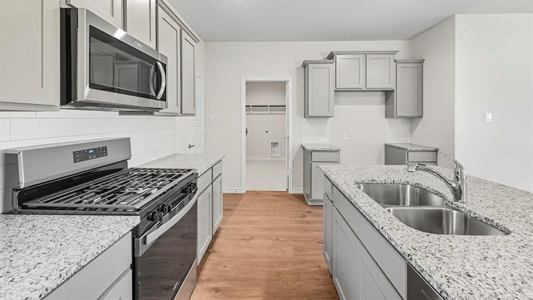 Kitchen featuring appliances with stainless steel finishes, gray cabinets, light stone counters, light wood finished floors, and decorative backsplash