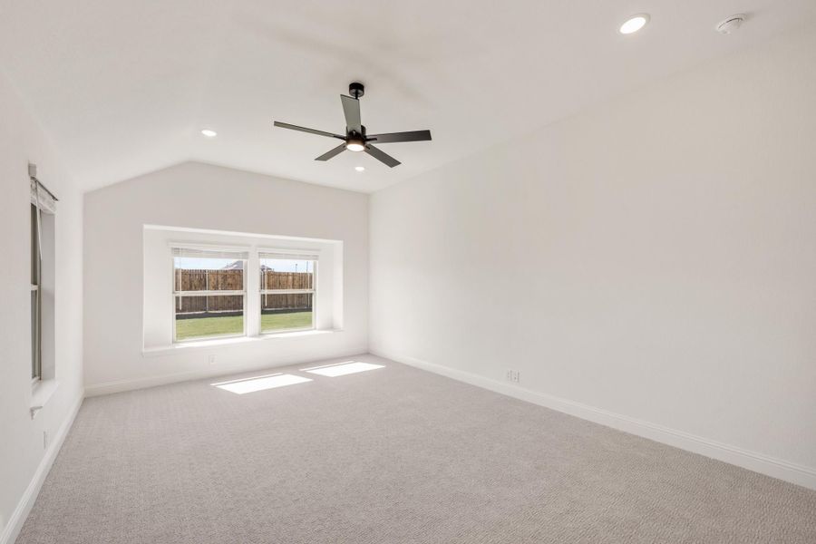 Empty bedroom with vaulted ceiling, ceiling fan, carpet flooring, and backyard-facing window Empty bedroom with vaulted ceiling, ceiling fan, carpet flooring, and backyard-facing window