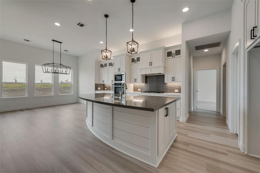 Kitchen with decorative light fixtures, backsplash, a kitchen island with sink, white cabinetry, and appliances with stainless steel finishes